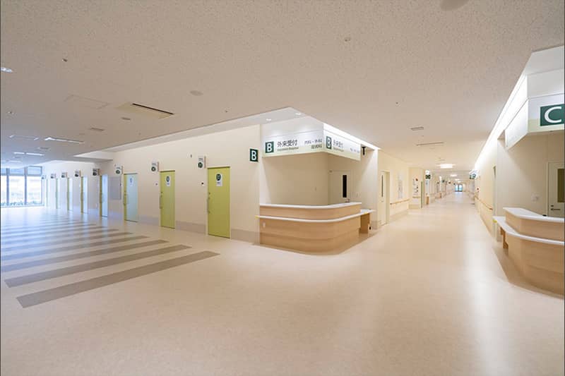 白を基調に薄黄緑のドアが並ぶ病棟の廊下の写真