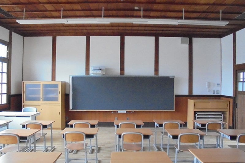 黒板を前に机が均等に並んでいる教室の写真